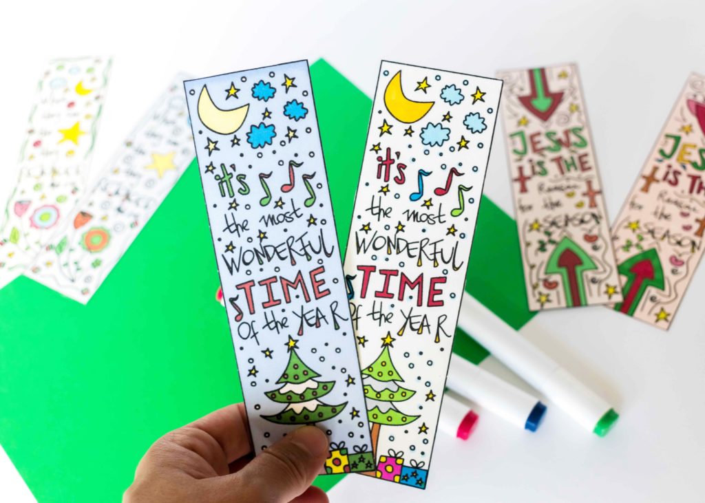 holding two Christmas bookmarks colored with markers