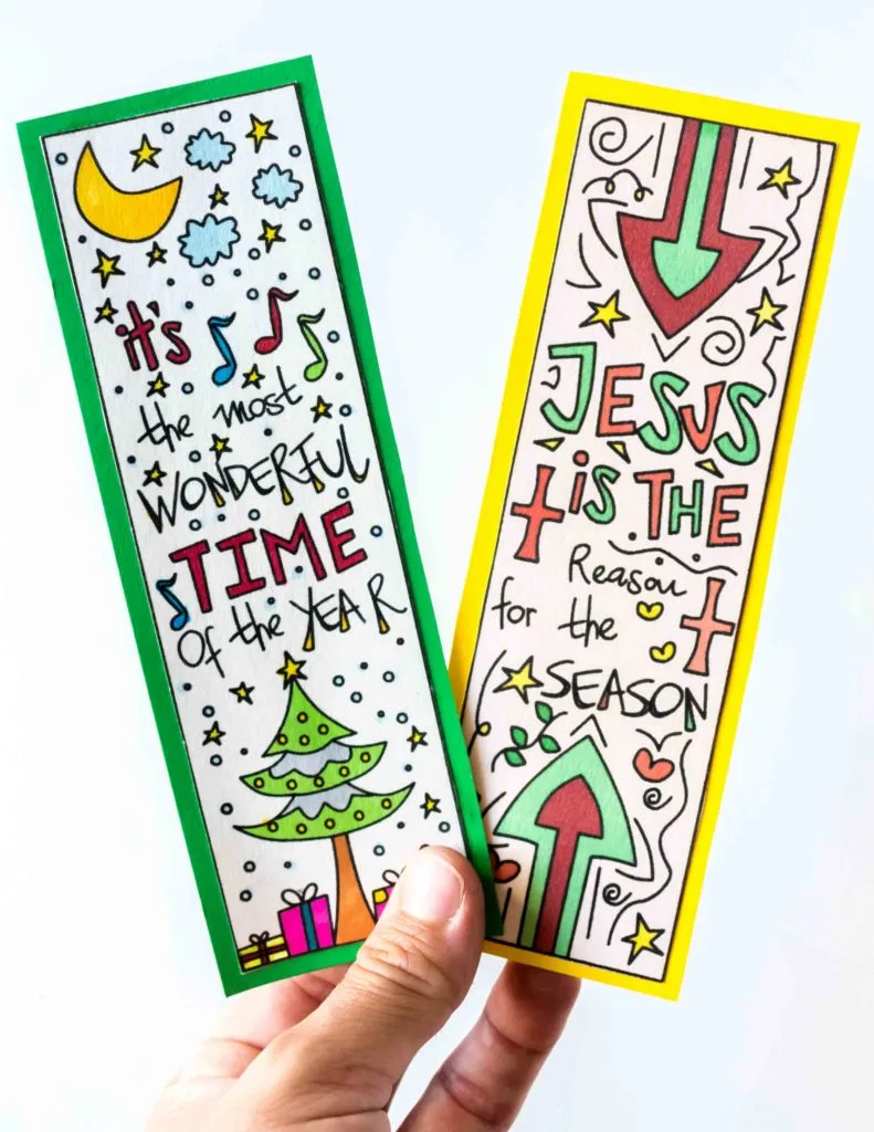 holding two colored hand drawn Christmas bookmarks