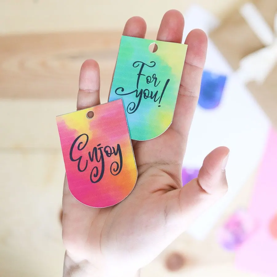 Holding watercolor gift tags that say "for you" and "enjoy"