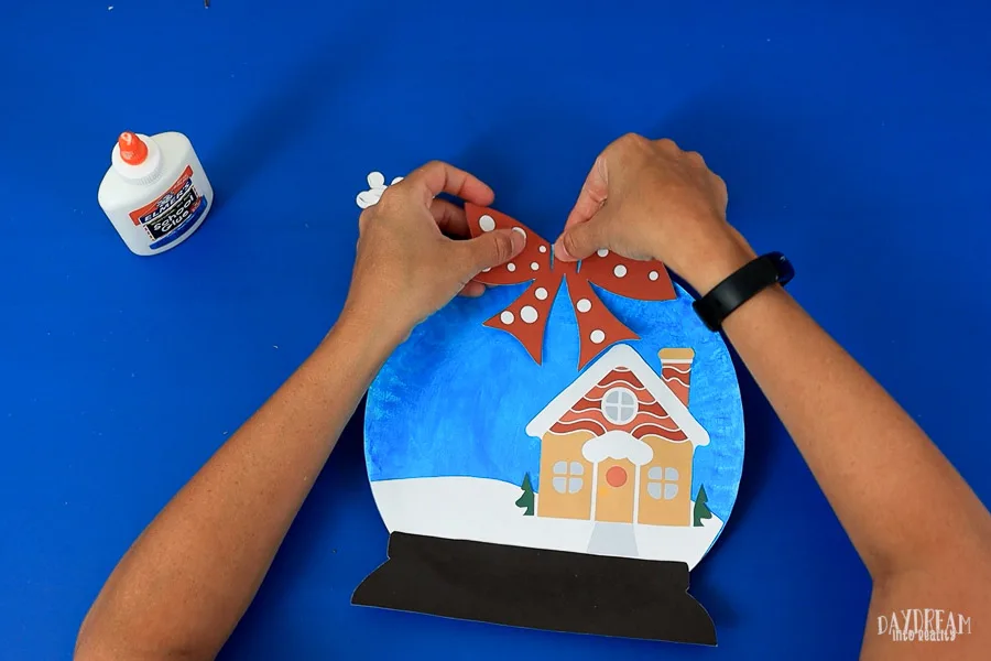 gluing bow on snow globe paper plate craft