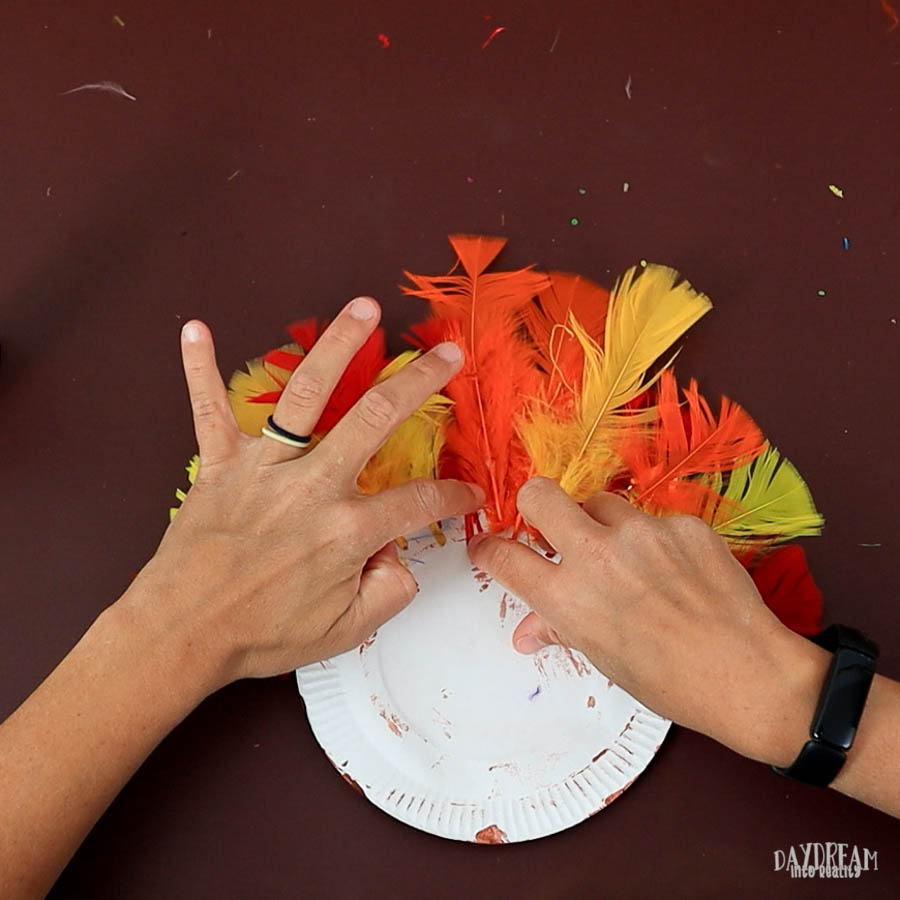 gluing feathers on paper plate turkey