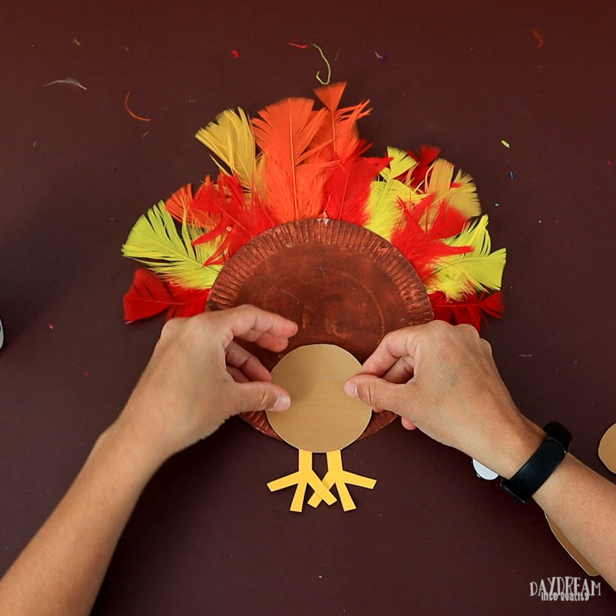 gluing head on paper plate turkey with feathers