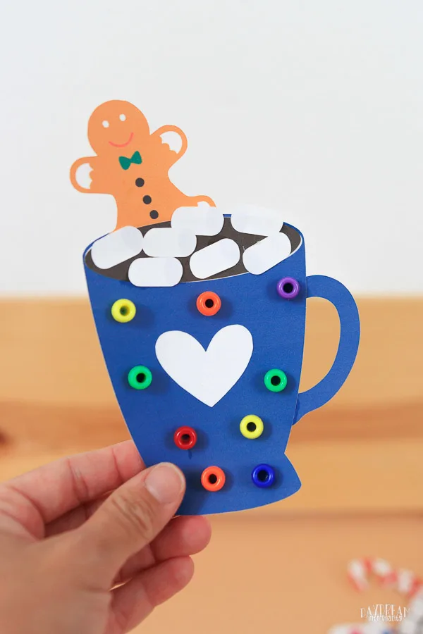 paper hot cocoa craft for kids - blue mug with beads, gingerbread man cookie and marshmallows.